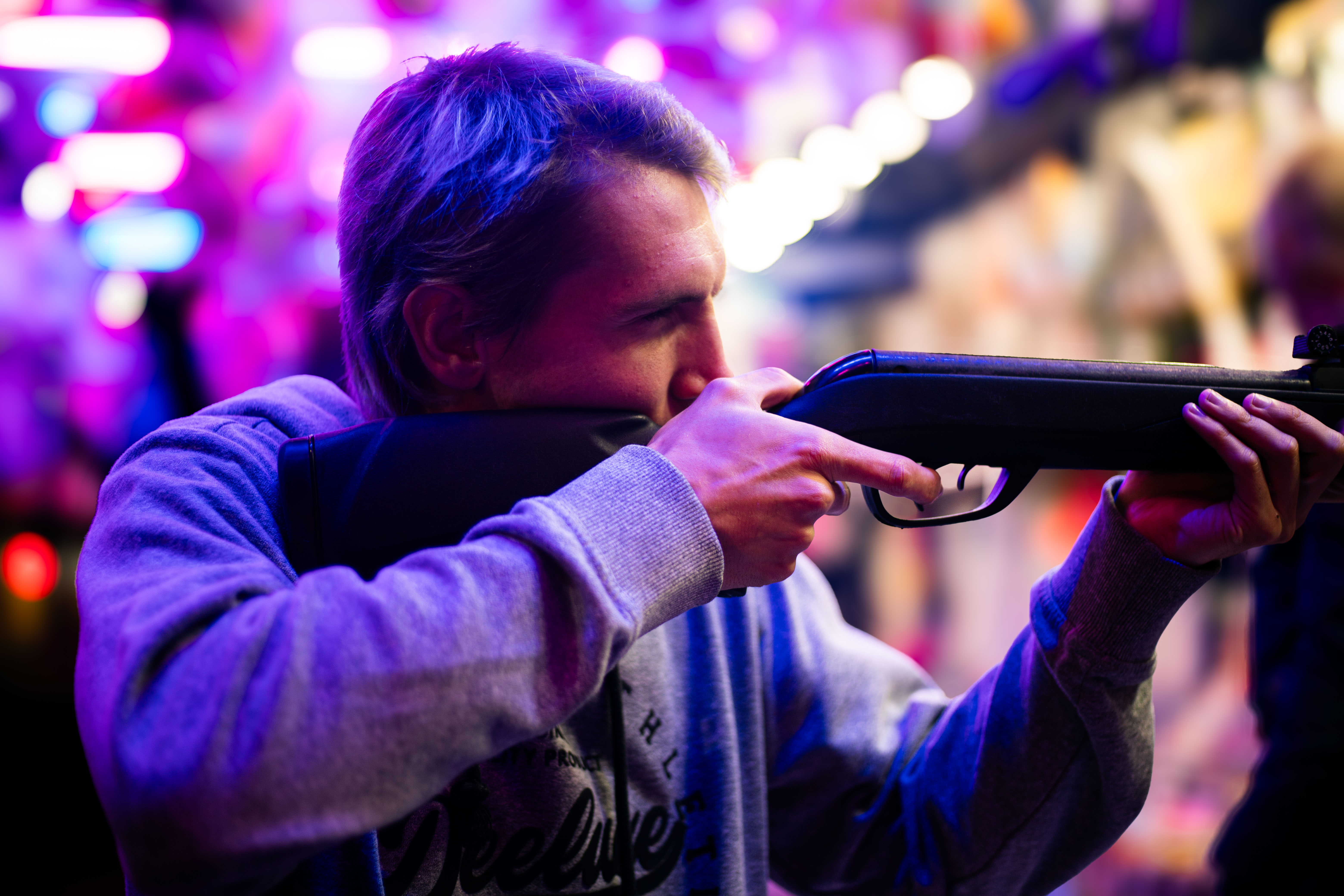 Photo d'un jeune homme de coté visant avec un fusil à air comprimé dans une fête foraine